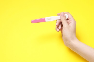 Woman holding pregnancy test on yellow background, closeup. Space for text