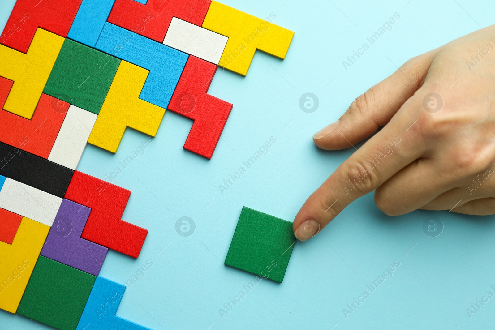 Photo of Woman playing with colorful wooden puzzle pieces on light blue background, top view