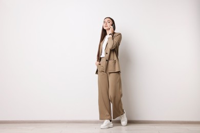 Photo of Woman in beige suit talking on smartphone indoors