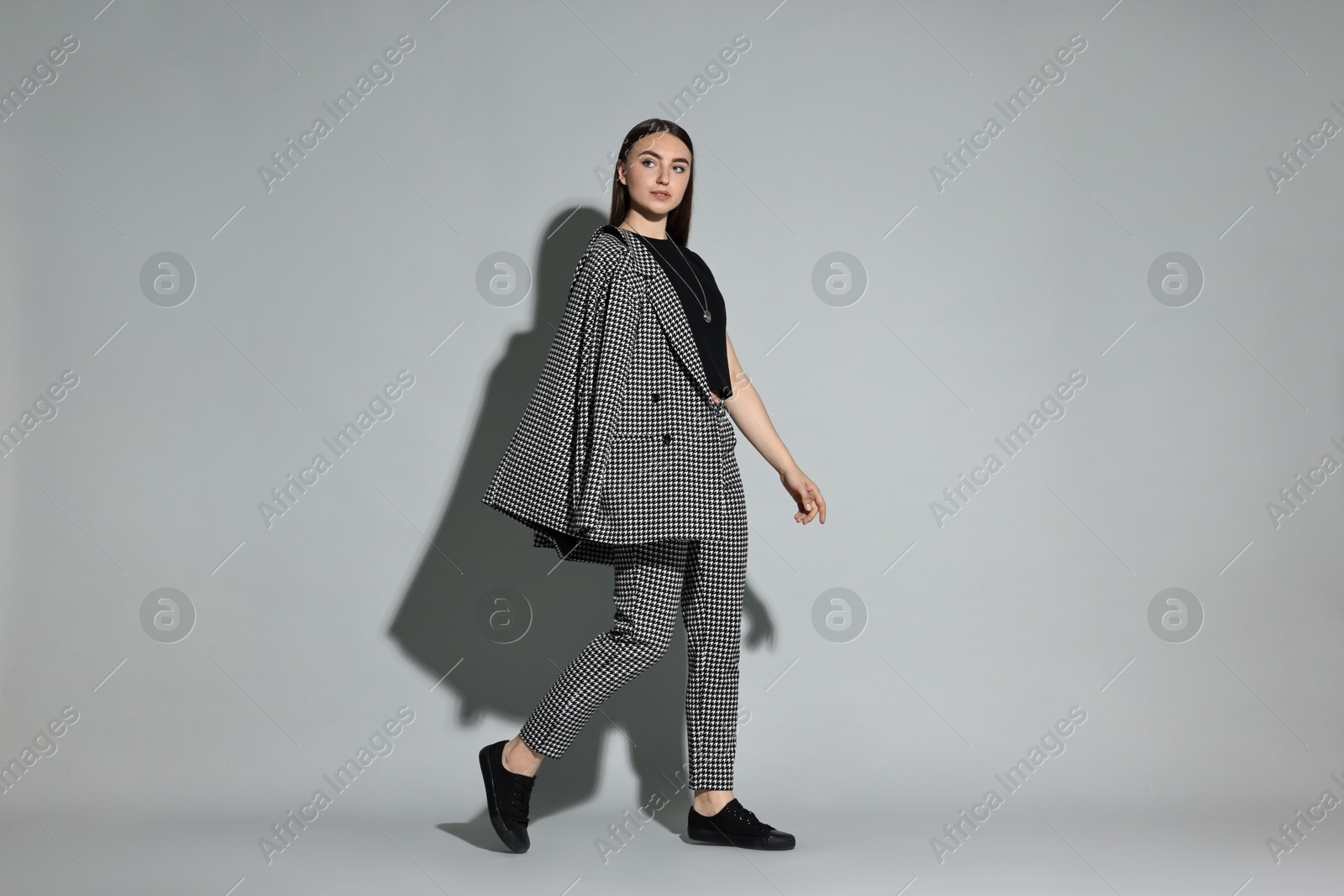 Photo of Beautiful woman in stylish suit walking on gray background