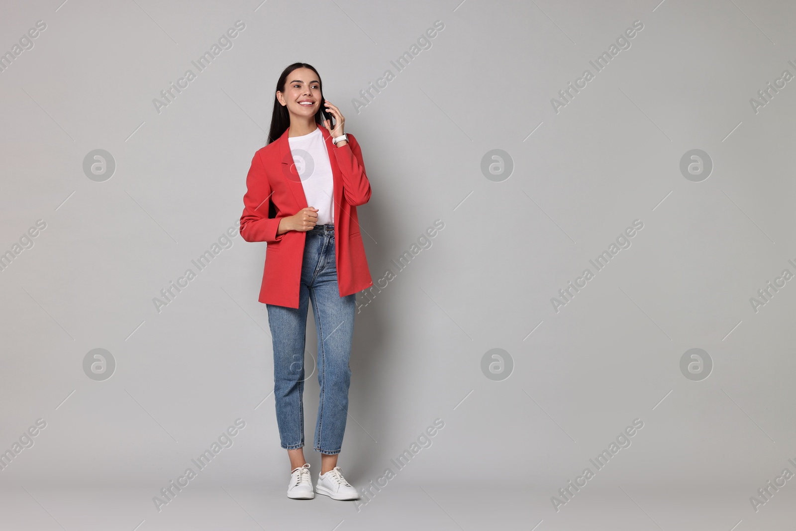 Photo of Beautiful woman in red jacket talking on phone against gray background, space for text