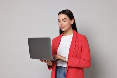 Photo of Beautiful woman in red jacket using laptop on gray background