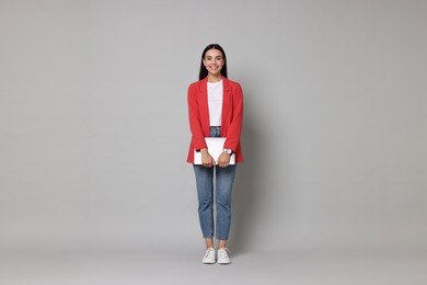 Beautiful woman in red jacket with laptop on gray background