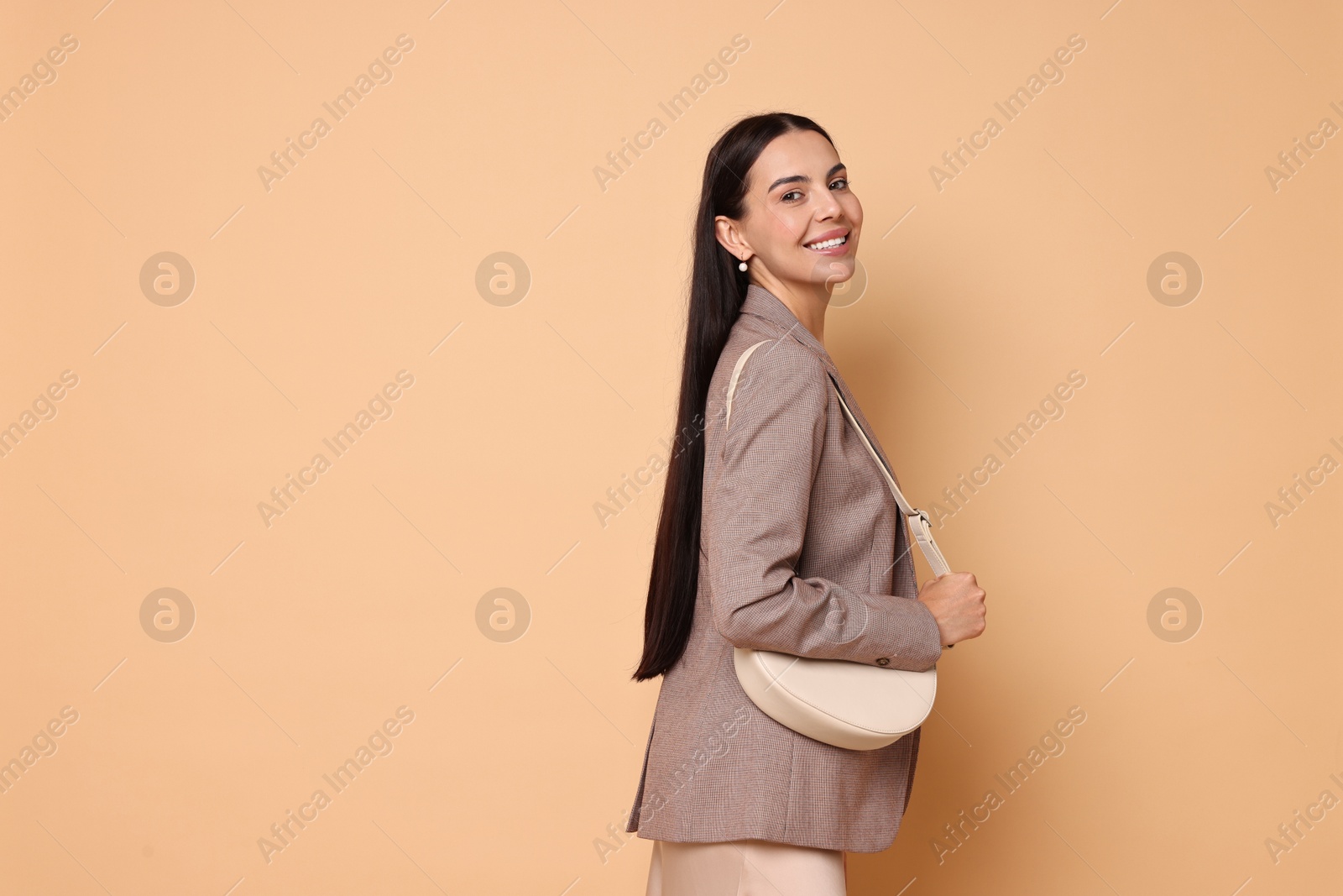 Photo of Beautiful woman in stylish jacket with bag on pale orange background, space for text