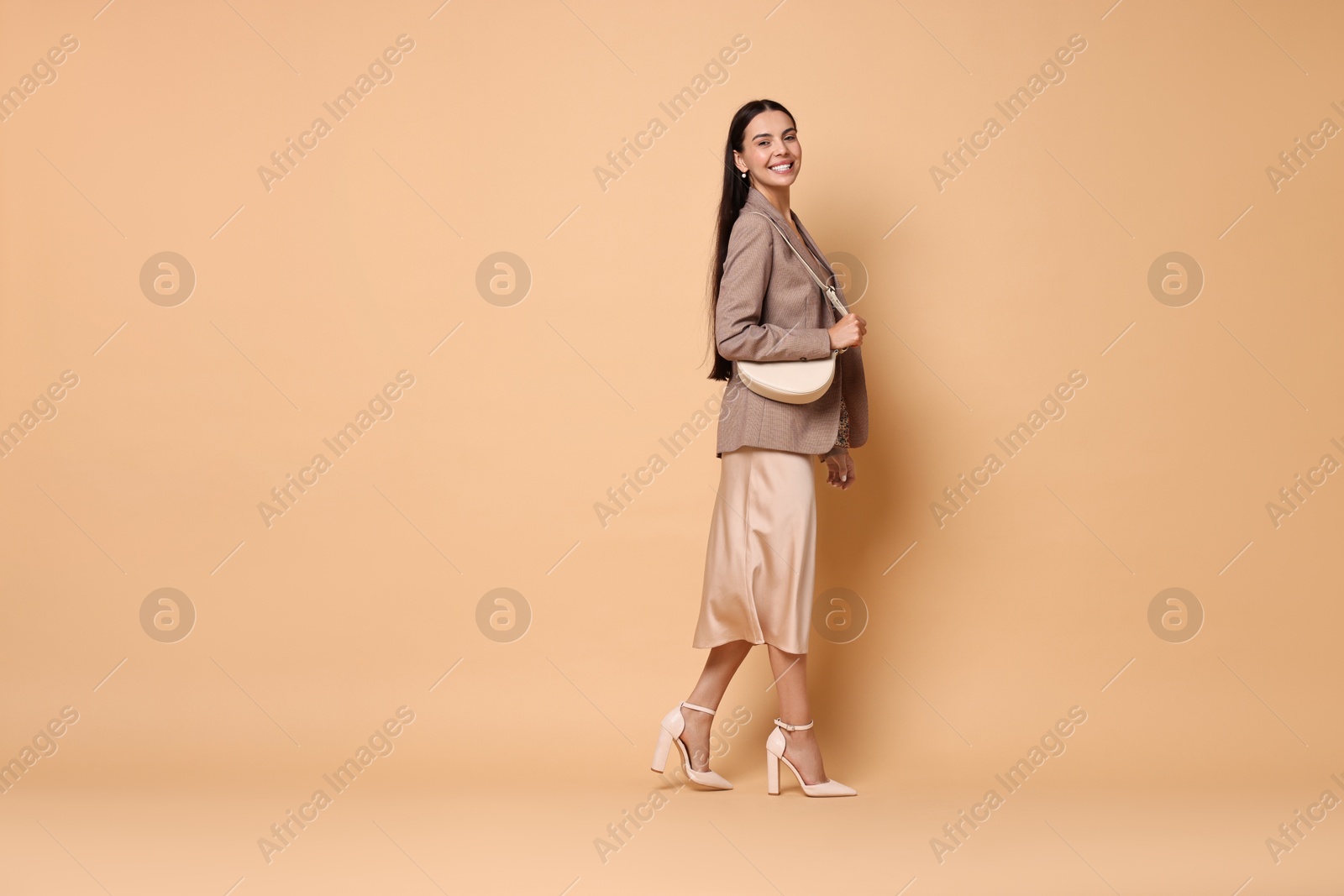 Photo of Beautiful woman in stylish jacket with bag on pale orange background