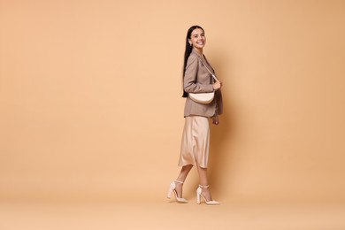 Photo of Beautiful woman in stylish jacket with bag on pale orange background