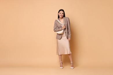 Photo of Beautiful woman in stylish jacket with bag on pale orange background