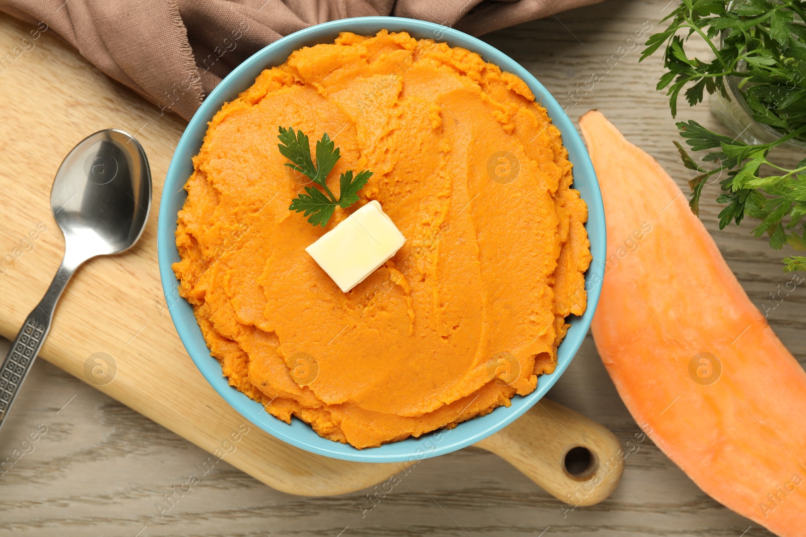 Photo of Tasty mashed sweet potato with butter and parsley in bowl served on wooden table, flat lay