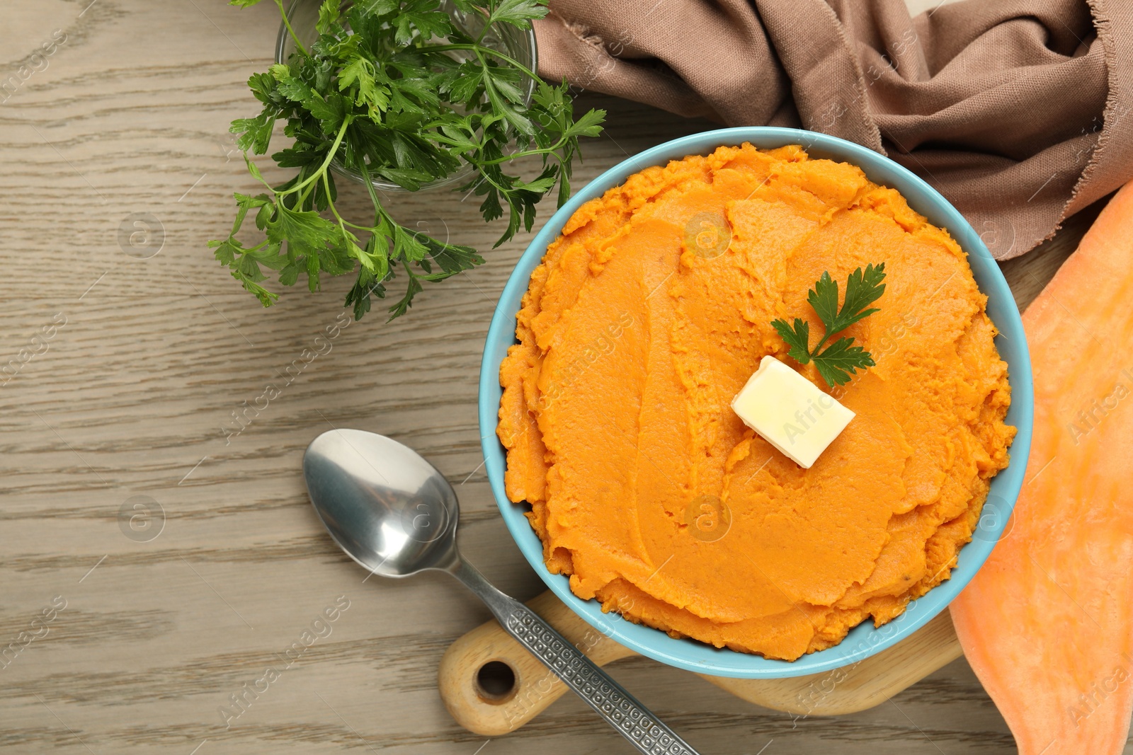 Photo of Tasty mashed sweet potato with butter and parsley in bowl served on wooden table, flat lay