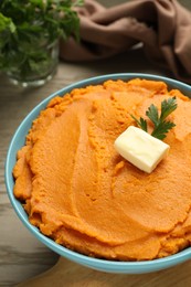 Tasty mashed sweet potato with butter and parsley in bowl on wooden table, closeup