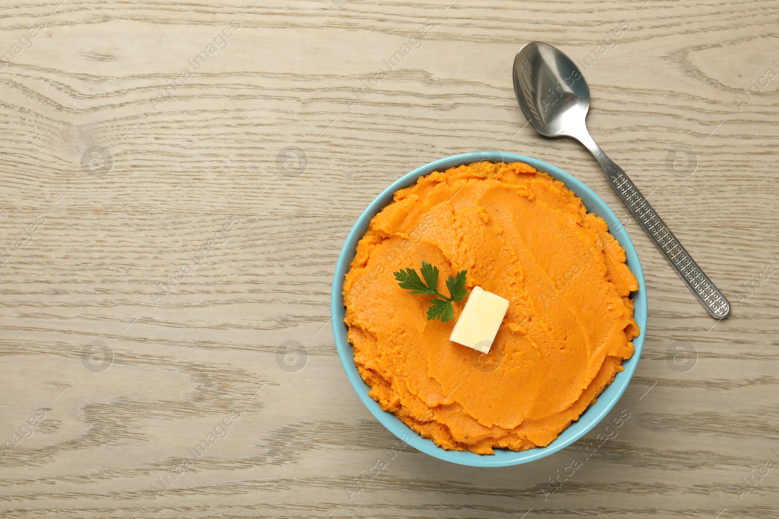 Photo of Tasty mashed sweet potato with butter and parsley in bowl on wooden table, top view. Space for text