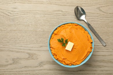 Tasty mashed sweet potato with butter and parsley in bowl on wooden table, top view. Space for text