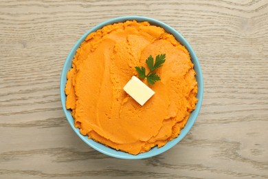 Photo of Tasty mashed sweet potato with butter and parsley in bowl on wooden table, top view