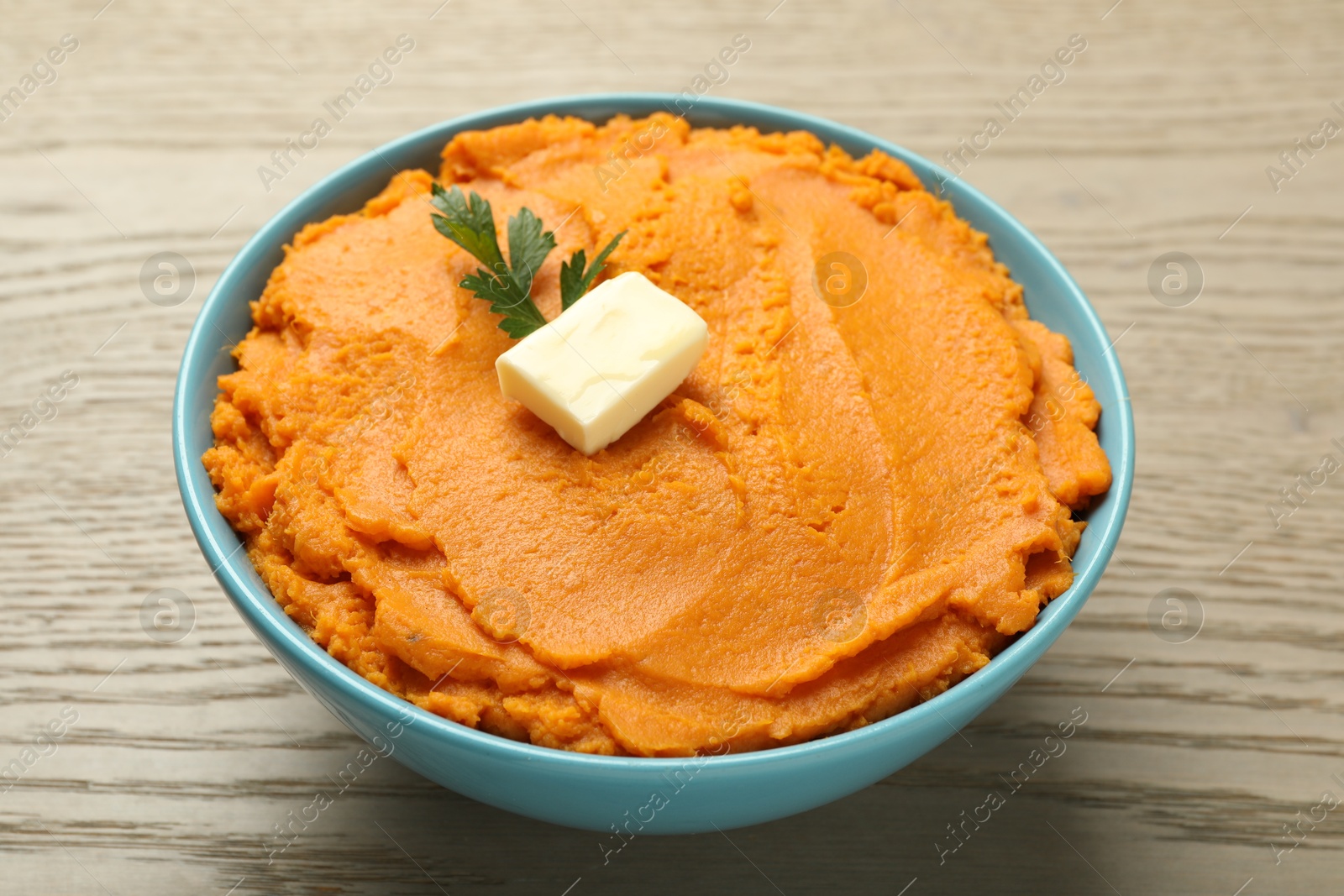 Photo of Tasty mashed sweet potato with butter and parsley in bowl on wooden table, closeup