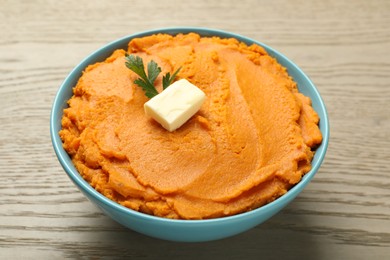 Tasty mashed sweet potato with butter and parsley in bowl on wooden table, closeup