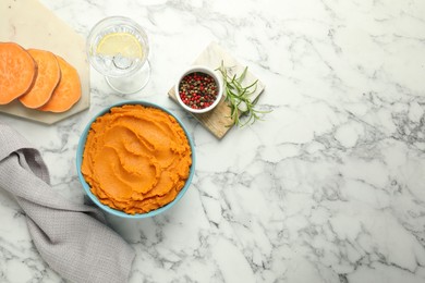 Tasty mashed sweet potato in bowl, peppercorns and water with lemon on white marble table, flat lay. Space for text