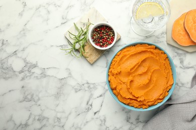 Tasty mashed sweet potato in bowl, peppercorns and water with lemon on white marble table, flat lay. Space for text