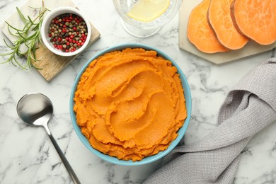 Tasty mashed sweet potato in bowl, peppercorns and rosemary served on white marble table, flat lay