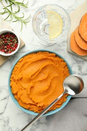 Photo of Tasty mashed sweet potato in bowl, peppercorns and rosemary served on white marble table, flat lay