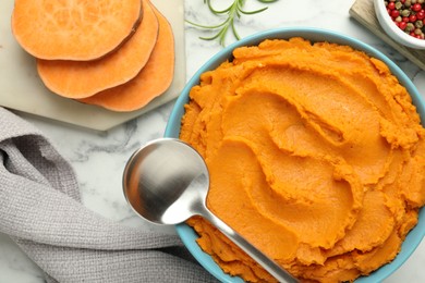 Photo of Tasty mashed sweet potato in bowl, peppercorns and rosemary served on white marble table, flat lay