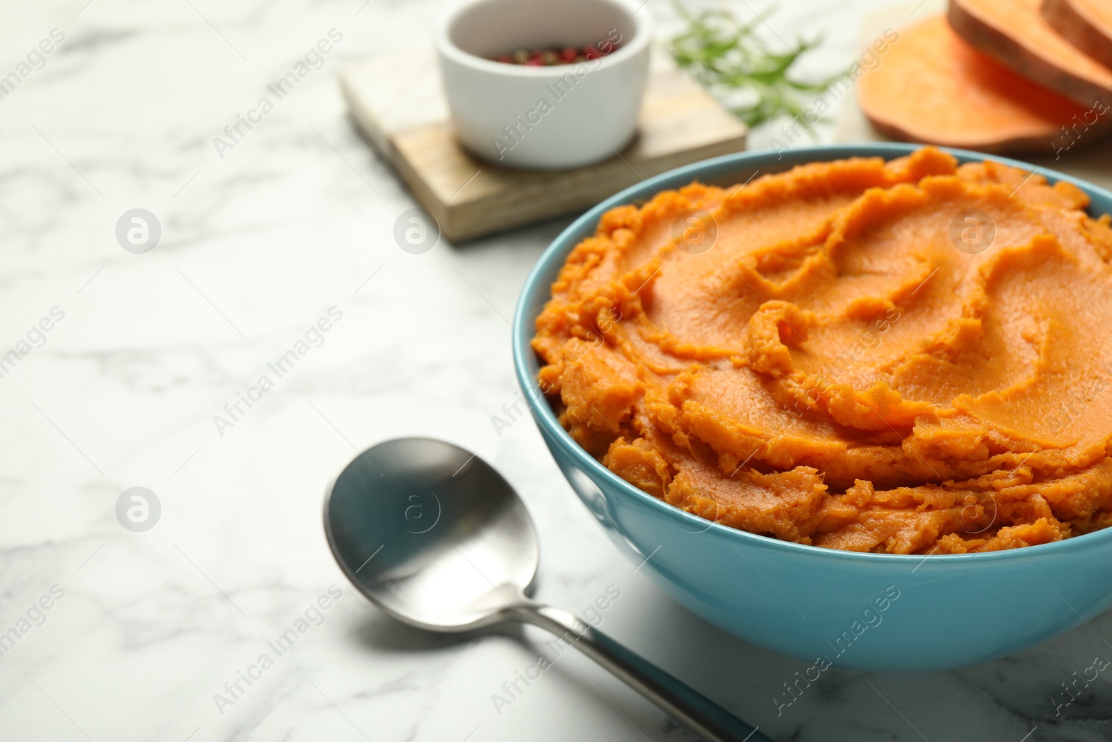 Photo of Tasty mashed sweet potato in bowl and spoon on white marble table, closeup. Space for text