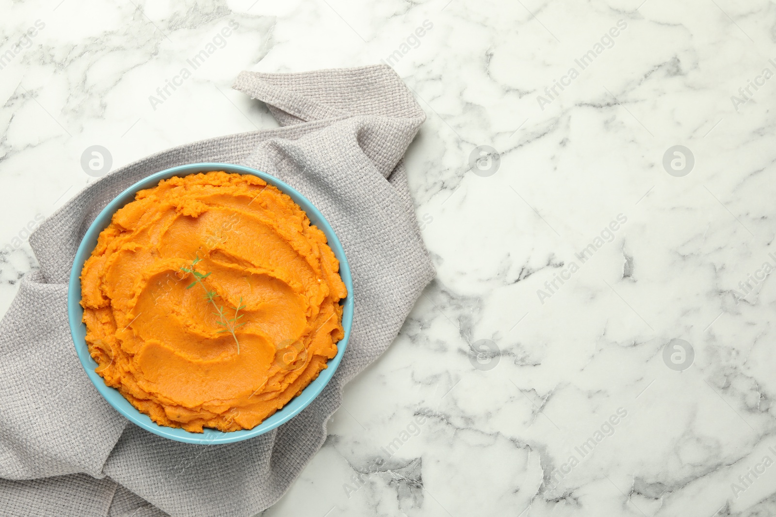 Photo of Tasty mashed sweet potato and thyme in bowl on white marble table, top view. Space for text