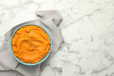 Tasty mashed sweet potato and thyme in bowl on white marble table, top view. Space for text