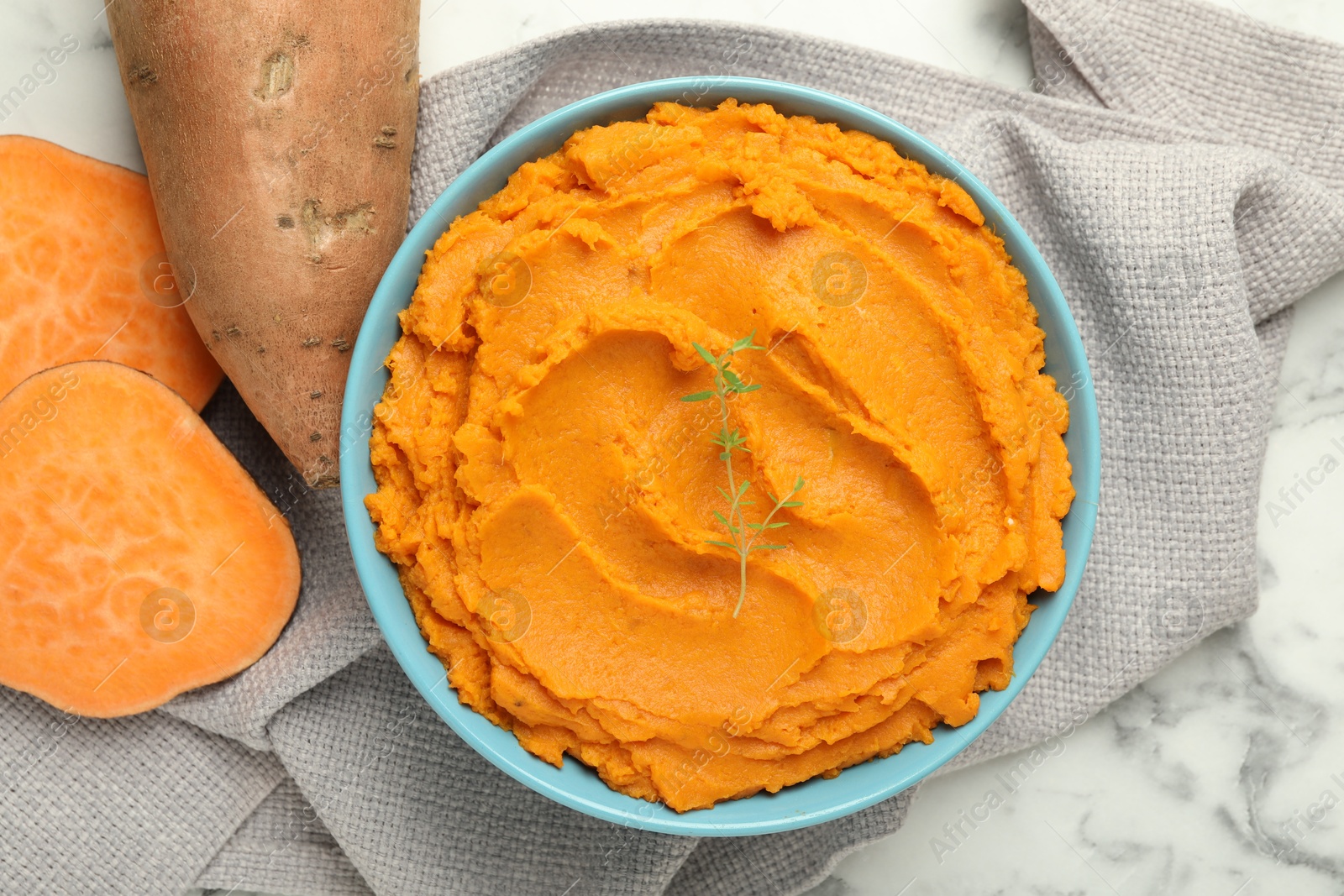 Photo of Tasty mashed sweet potato and thyme in bowl on white marble table, flat lay