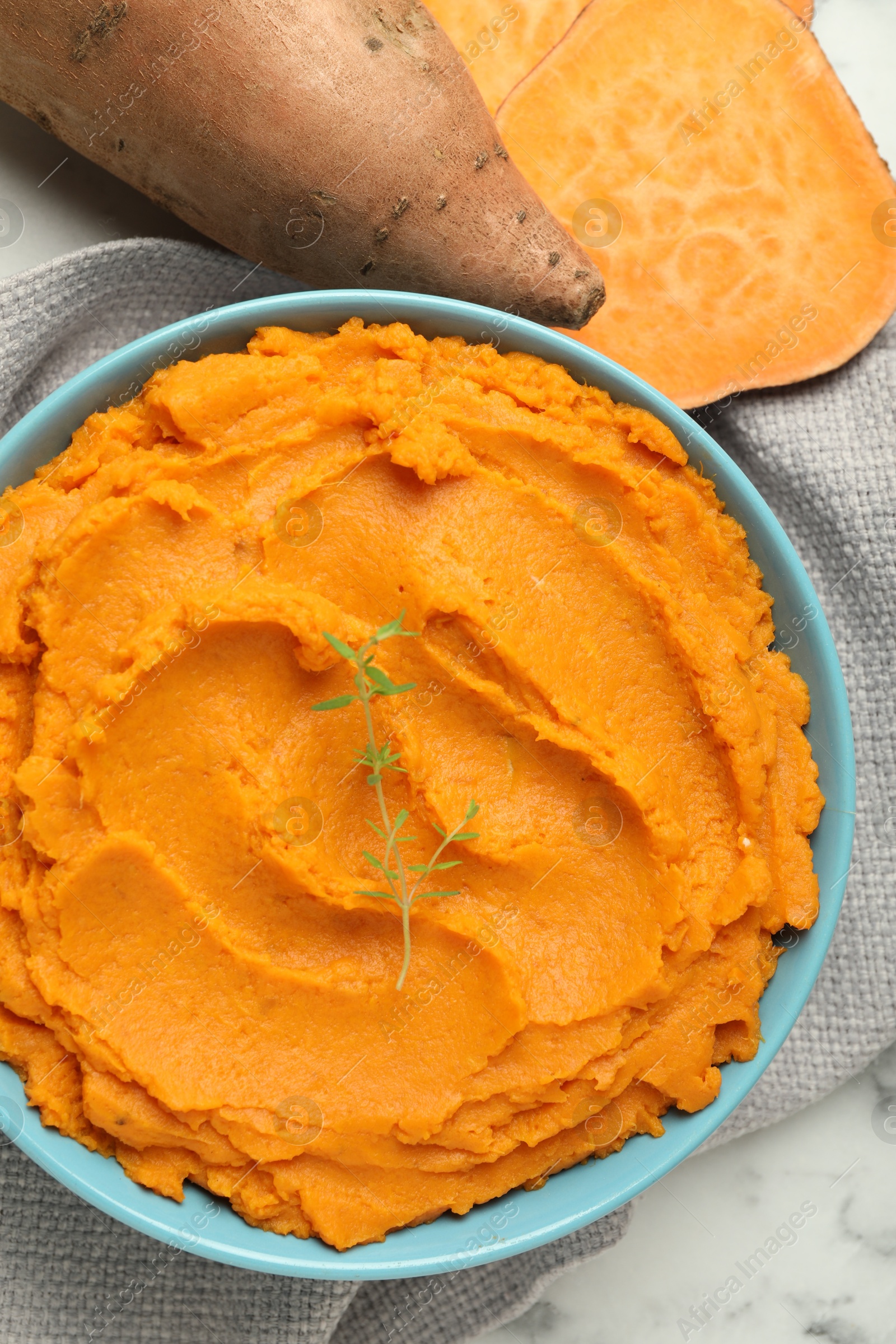 Photo of Tasty mashed sweet potato and thyme in bowl on white marble table, flat lay