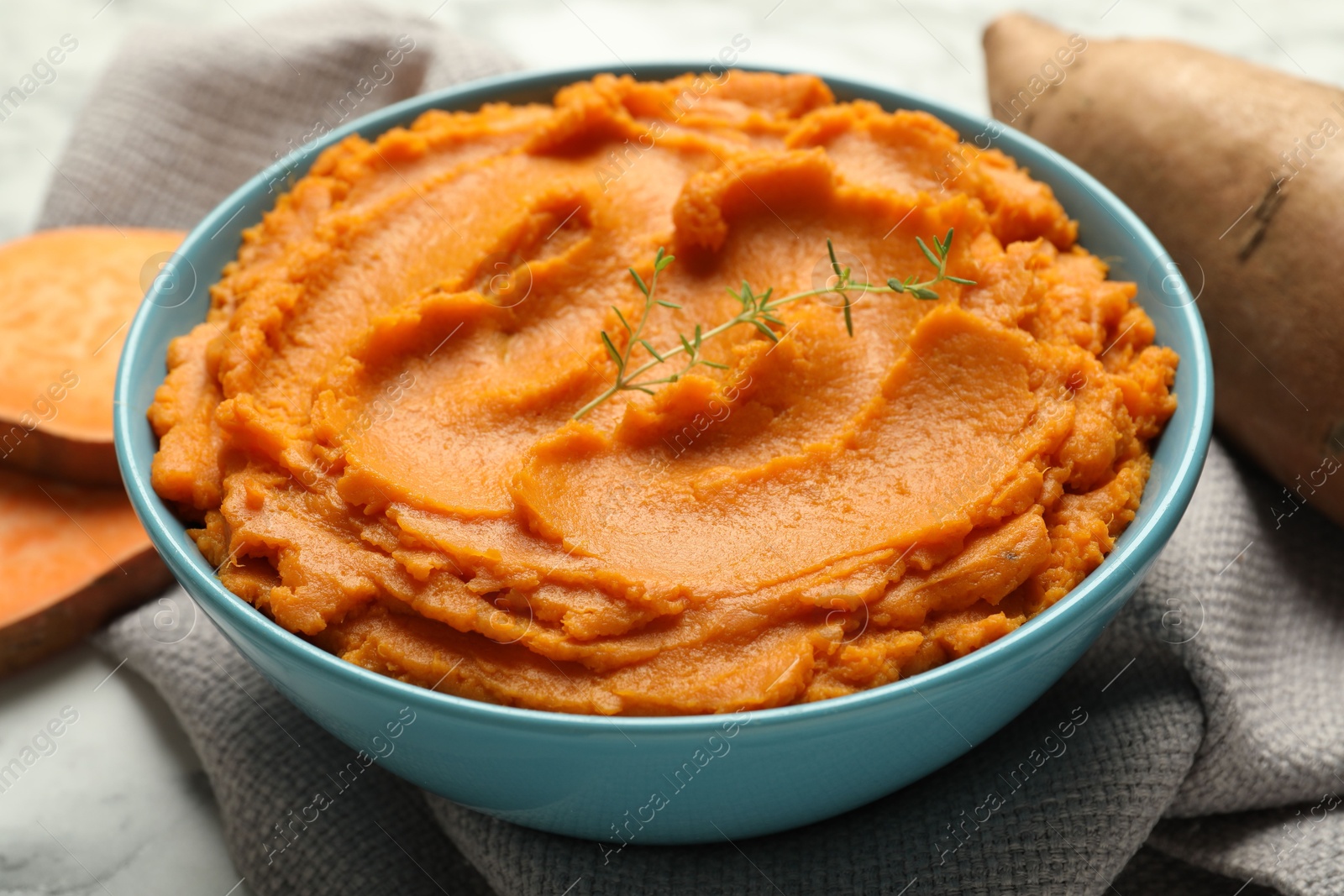 Photo of Tasty mashed sweet potato and thyme in bowl on table, closeup