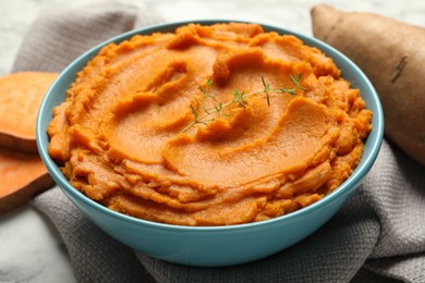 Photo of Tasty mashed sweet potato and thyme in bowl on table, closeup