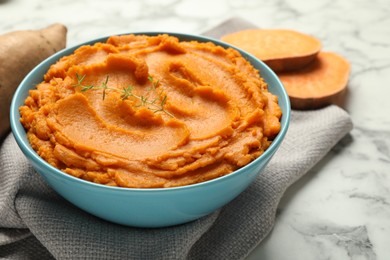 Photo of Tasty mashed sweet potato and thyme in bowl on white marble table, closeup