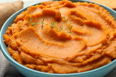 Photo of Tasty mashed sweet potato and thyme in bowl on table, closeup