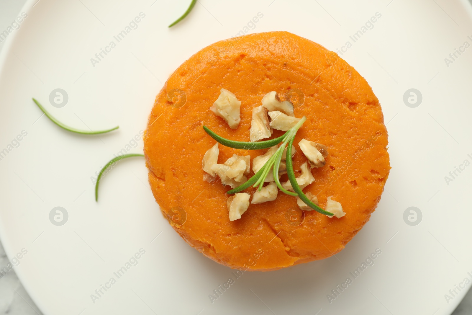 Photo of Tasty mashed sweet potato, rosemary and walnuts on plate, top view