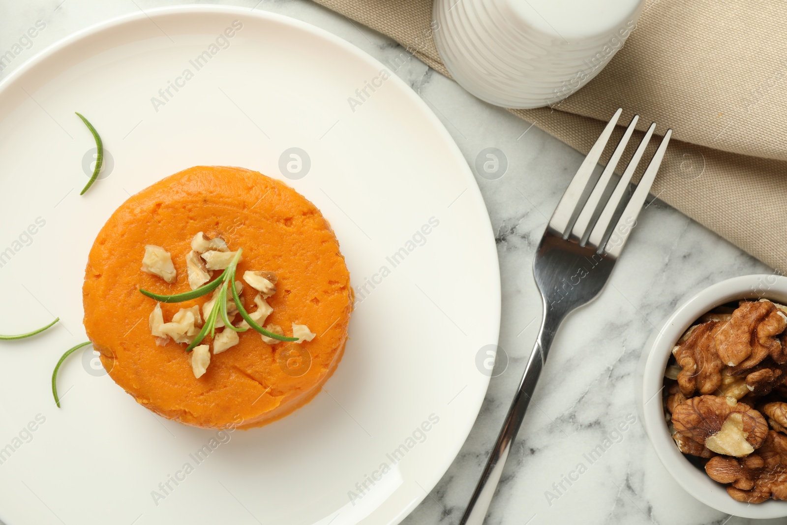 Photo of Tasty mashed sweet potato, rosemary and walnuts served on white marble table, flat lay