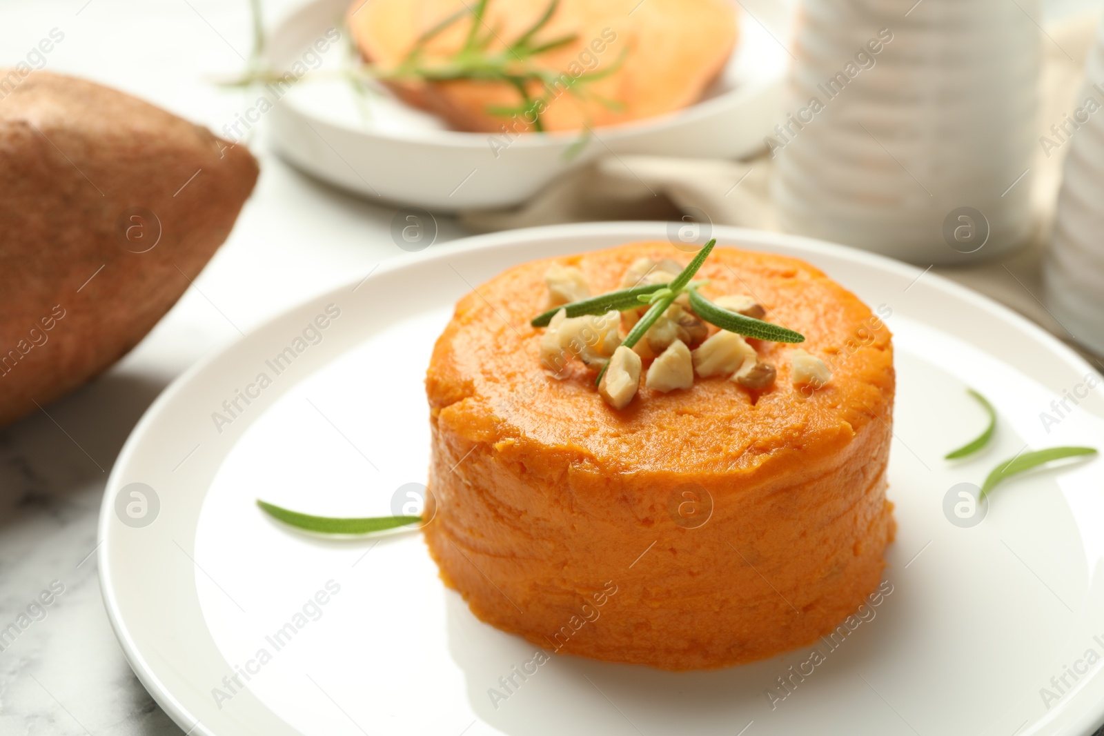 Photo of Plate with tasty mashed sweet potato, rosemary and walnuts on white marble table, closeup