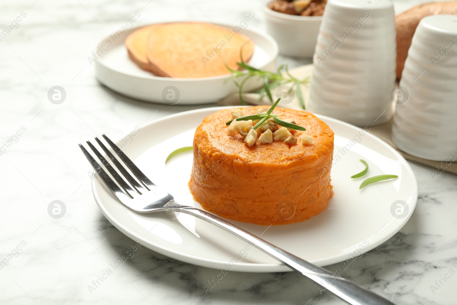 Photo of Plate with tasty mashed sweet potato, rosemary and walnuts on white marble table, closeup