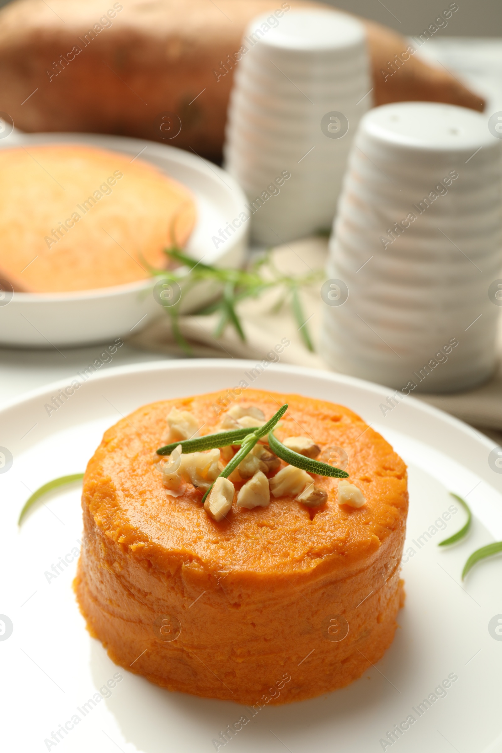 Photo of Plate with tasty mashed sweet potato, rosemary and walnuts on table, closeup