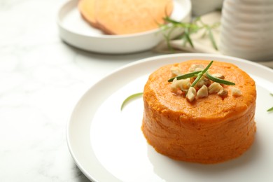 Photo of Plate with tasty mashed sweet potato, rosemary and walnuts on white table, closeup