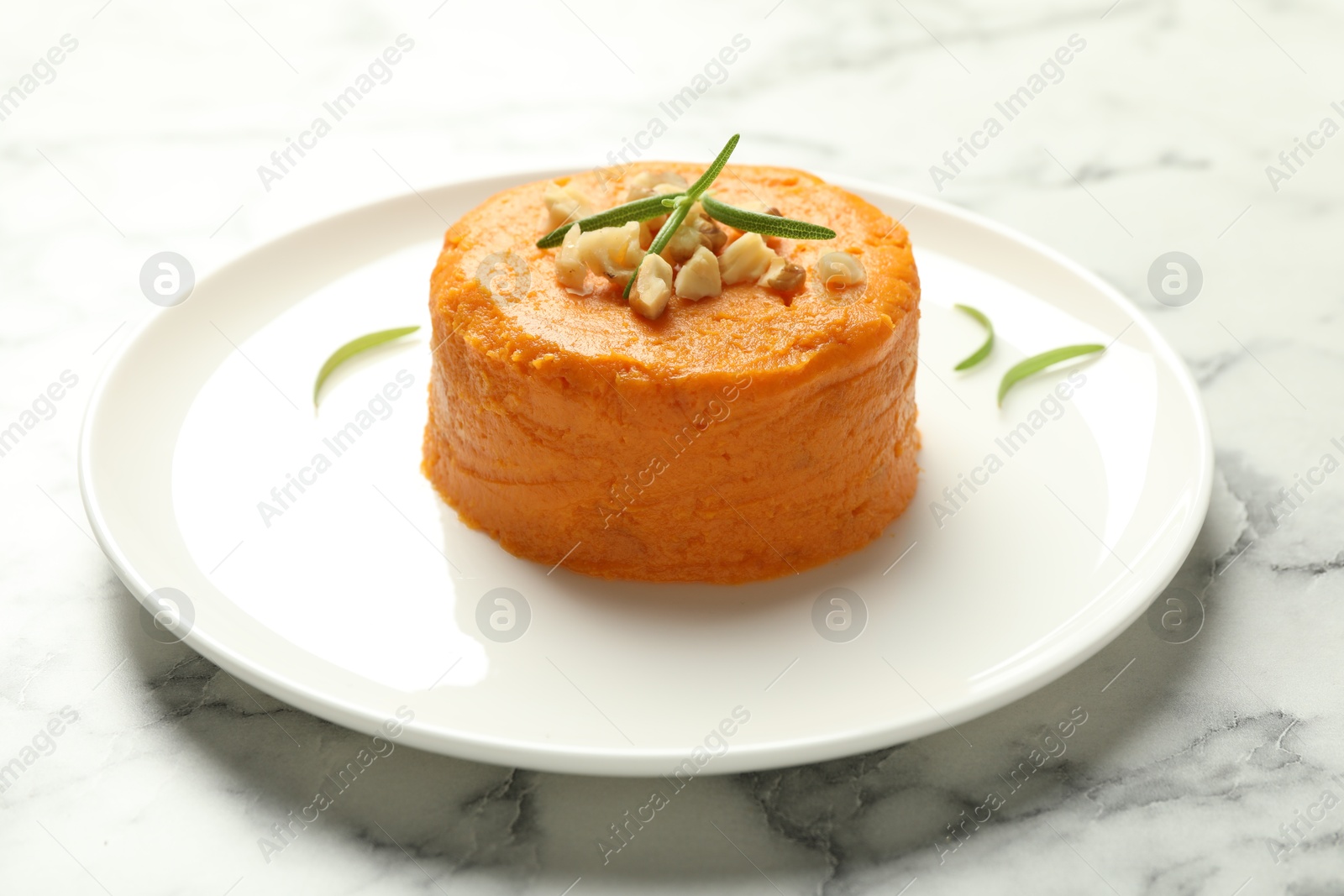 Photo of Plate with tasty mashed sweet potato, rosemary and walnuts on white marble table, closeup