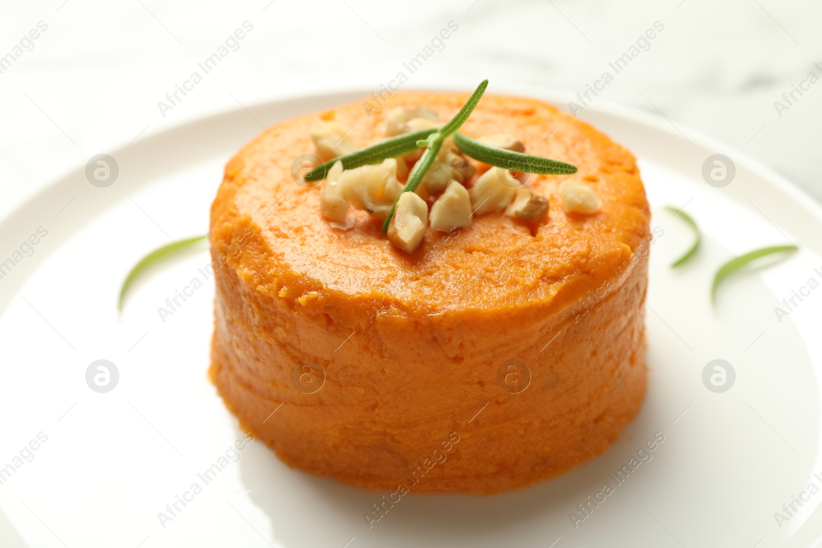 Photo of Plate with tasty mashed sweet potato, rosemary and walnuts on table, closeup