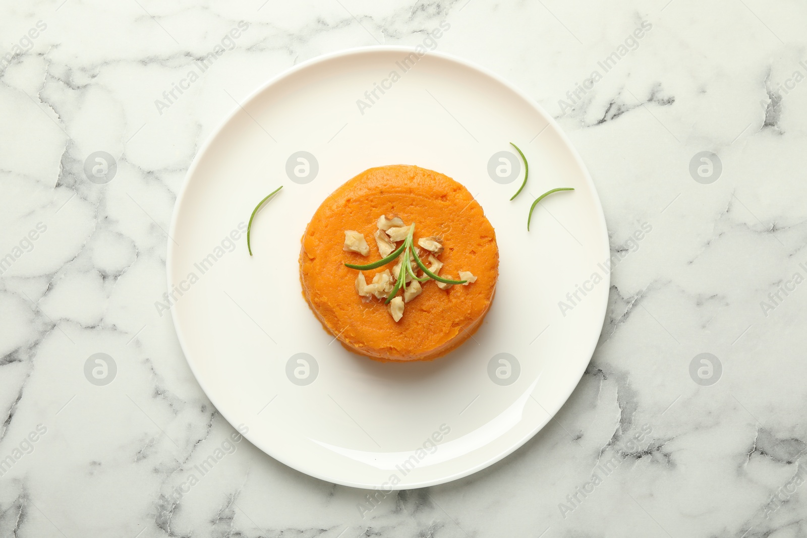 Photo of Plate with tasty mashed sweet potato, rosemary and walnuts on white marble table, top view