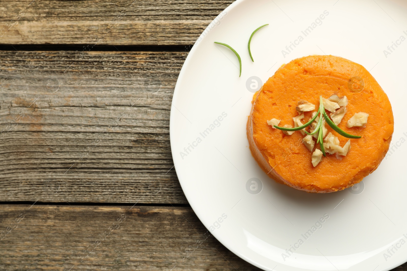 Photo of Plate with tasty mashed sweet potato, rosemary and walnuts on wooden table, top view. Space for text