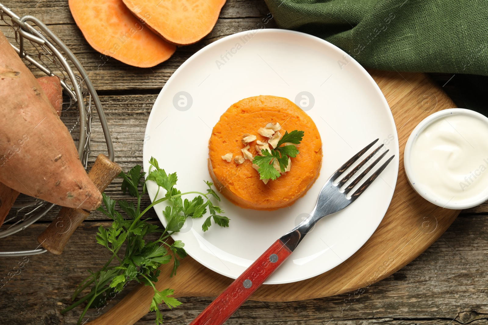 Photo of Tasty mashed sweet potato, parsley and walnuts served with sauce on wooden table, flat lay