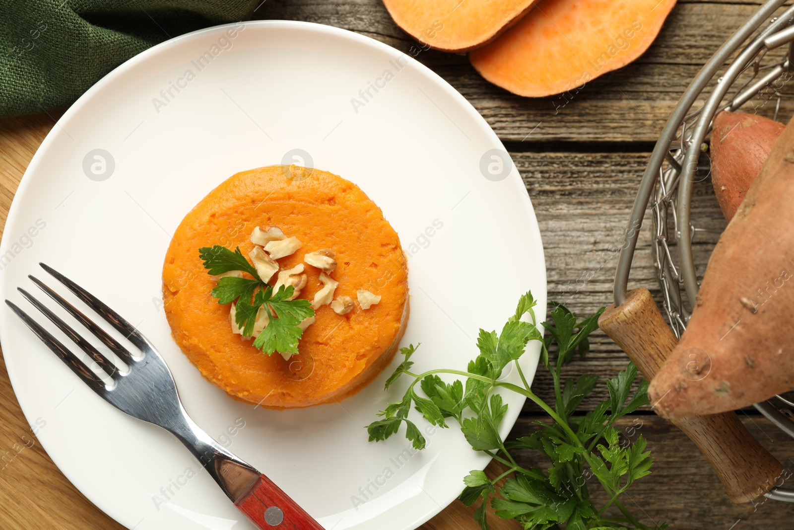 Photo of Tasty mashed sweet potato, parsley and walnuts served on wooden table, flat lay