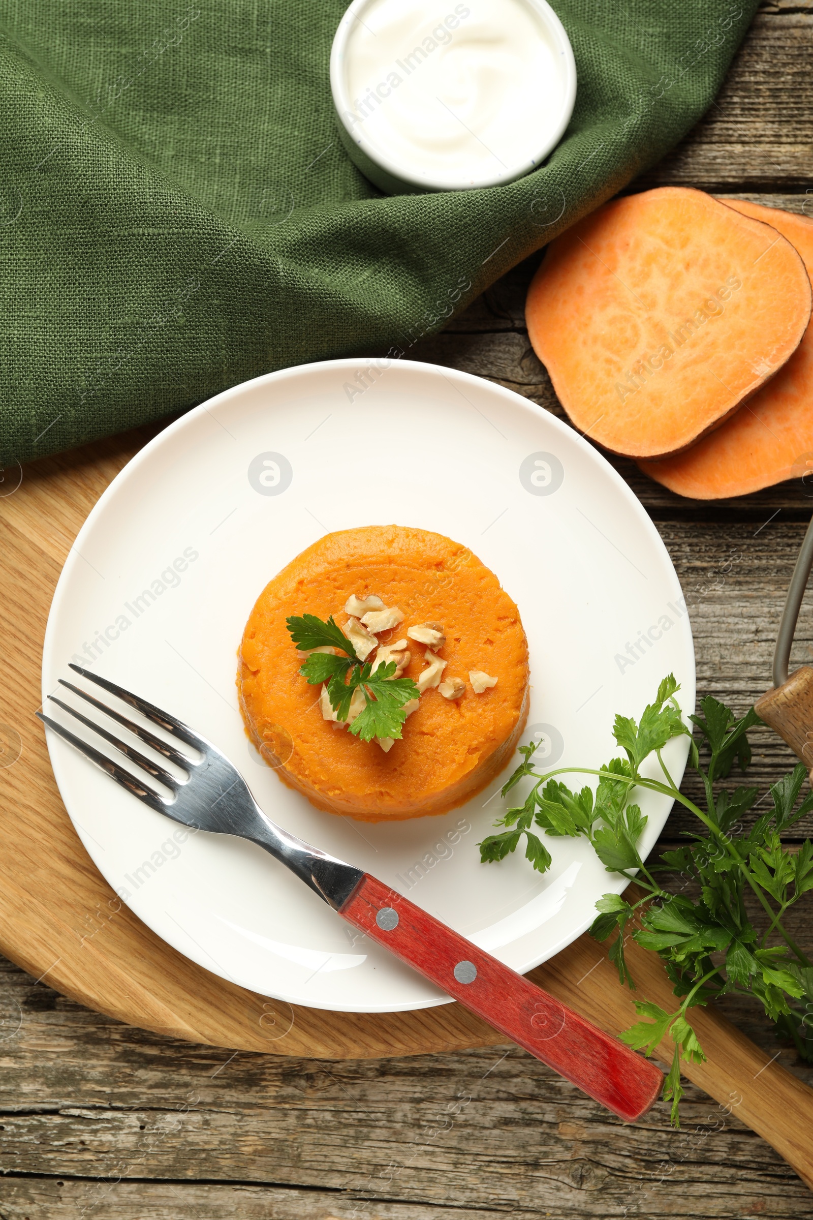 Photo of Tasty mashed sweet potato, parsley and walnuts served with sauce on wooden table, flat lay