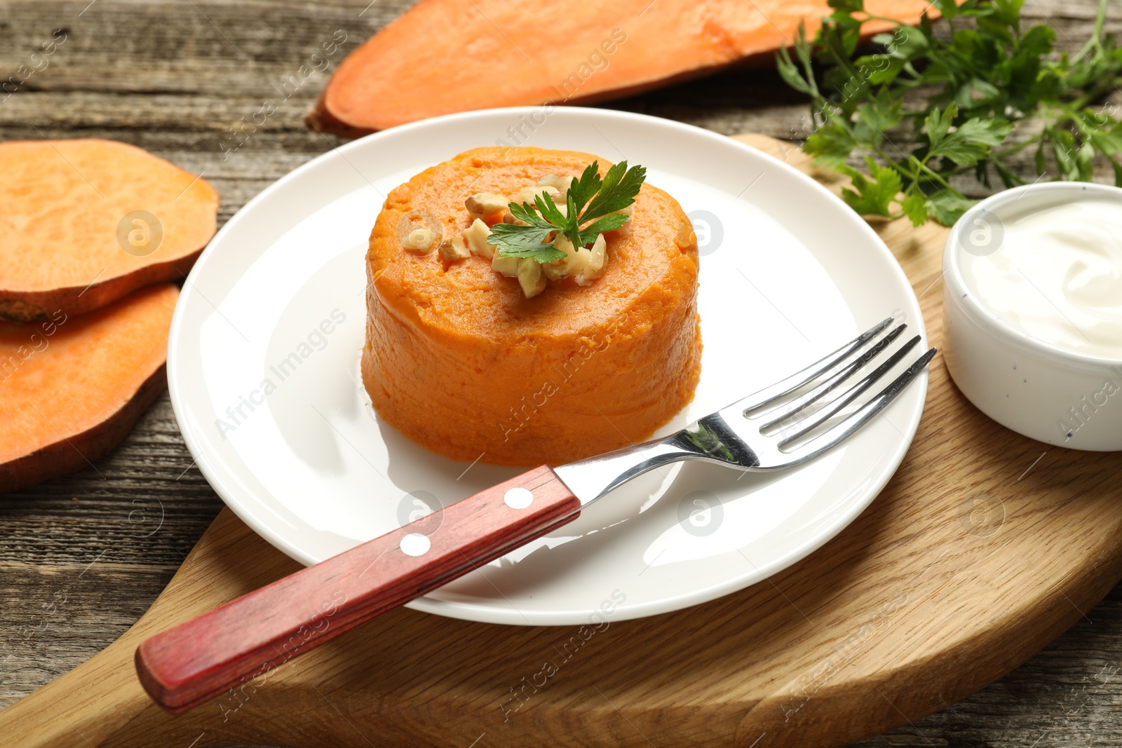 Photo of Tasty mashed sweet potato, parsley and walnuts served with sauce on wooden table, closeup