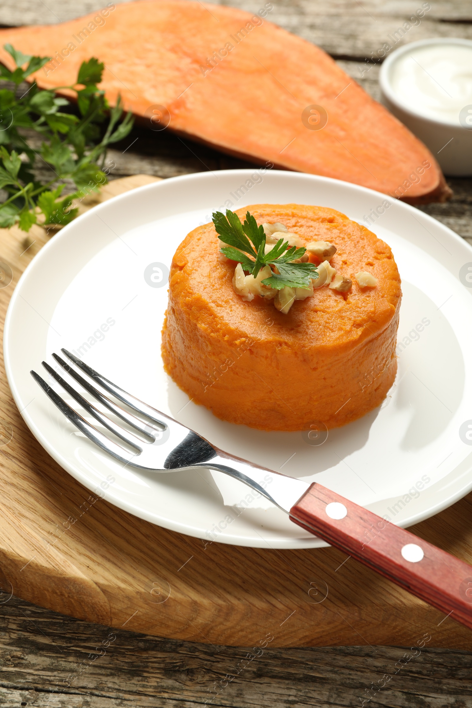 Photo of Tasty mashed sweet potato, parsley and walnuts served on wooden table, closeup