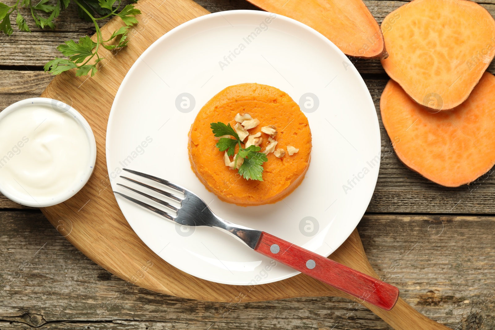 Photo of Tasty mashed sweet potato, parsley and walnuts served with sauce on wooden table, flat lay