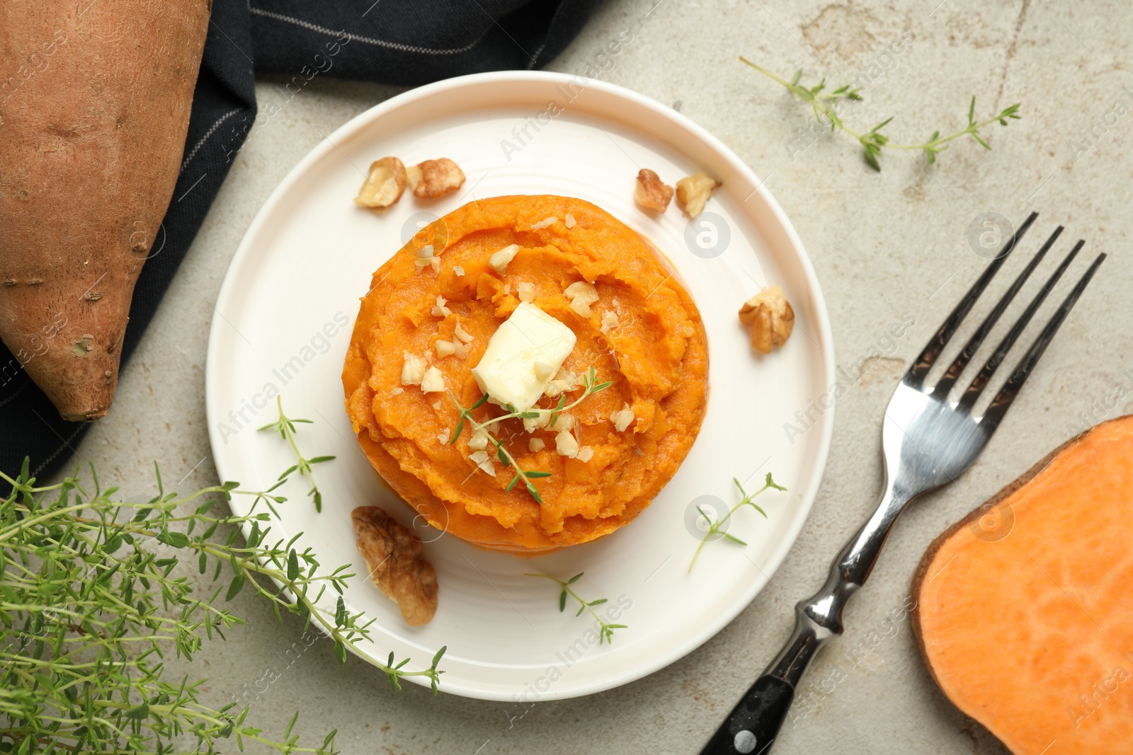 Photo of Tasty mashed sweet potato, butter, thyme and walnuts served on grey textured table, flat lay